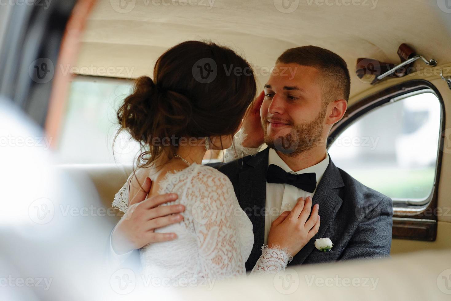 Beautiful happy young bride and groom looking from retro auto photo