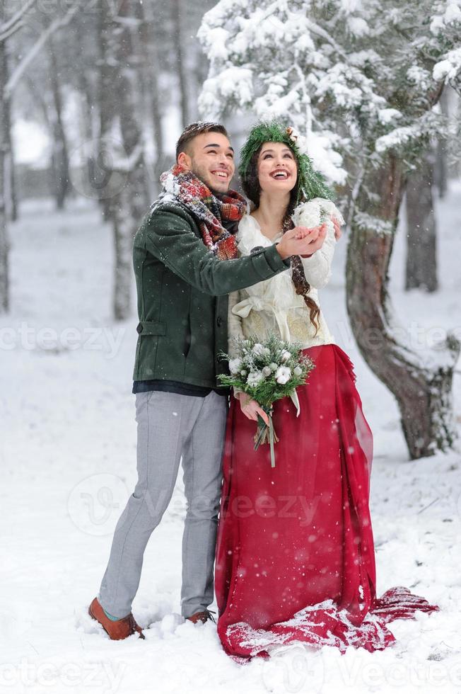 Beautiful bride and groom with a white dog are standing on the background of a snowy forest. photo