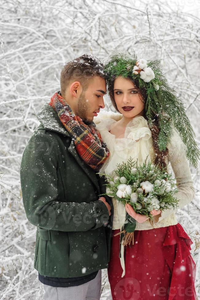 Beautiful bride and groom with a white dog are standing on the background of a snowy forest. photo