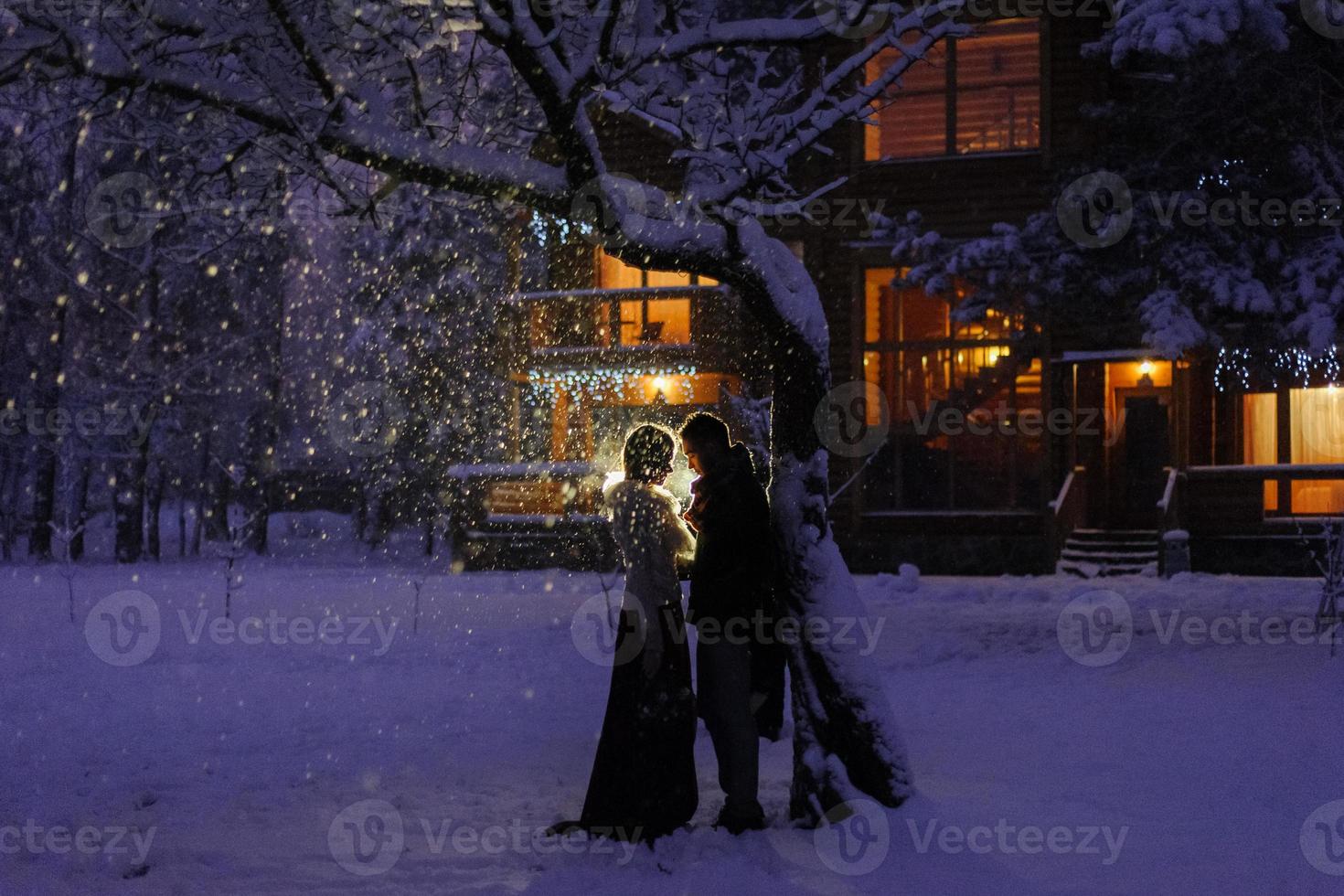 hermosa novia y novio con un perro blanco están parados en el fondo de un bosque nevado. foto