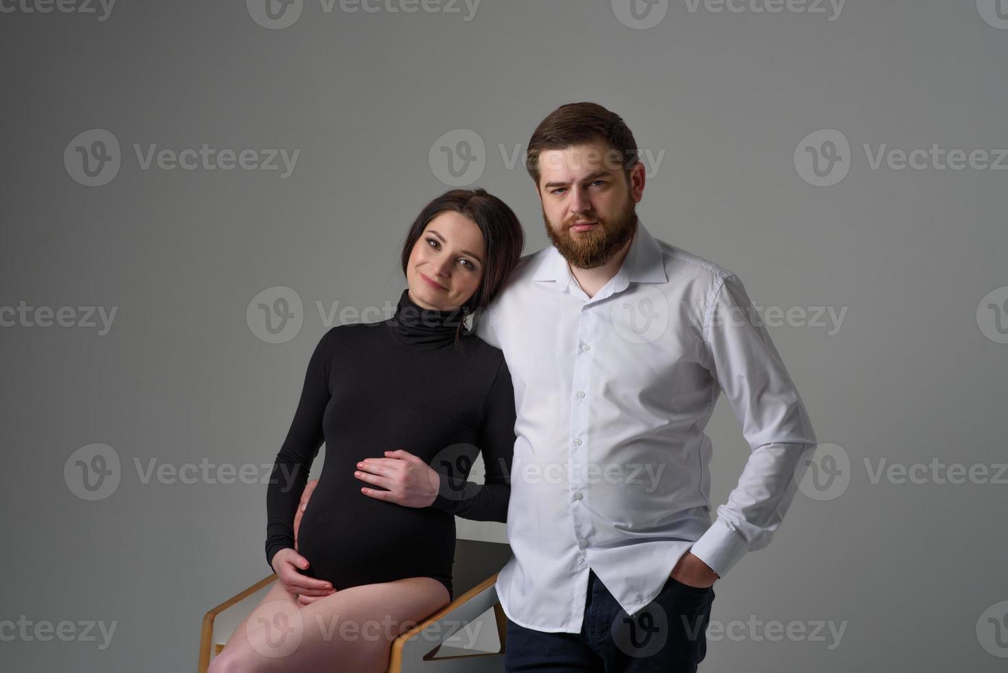 una mujer embarazada y su esposo se abrazan en un fondo gris. pareja esperando un bebé. foto