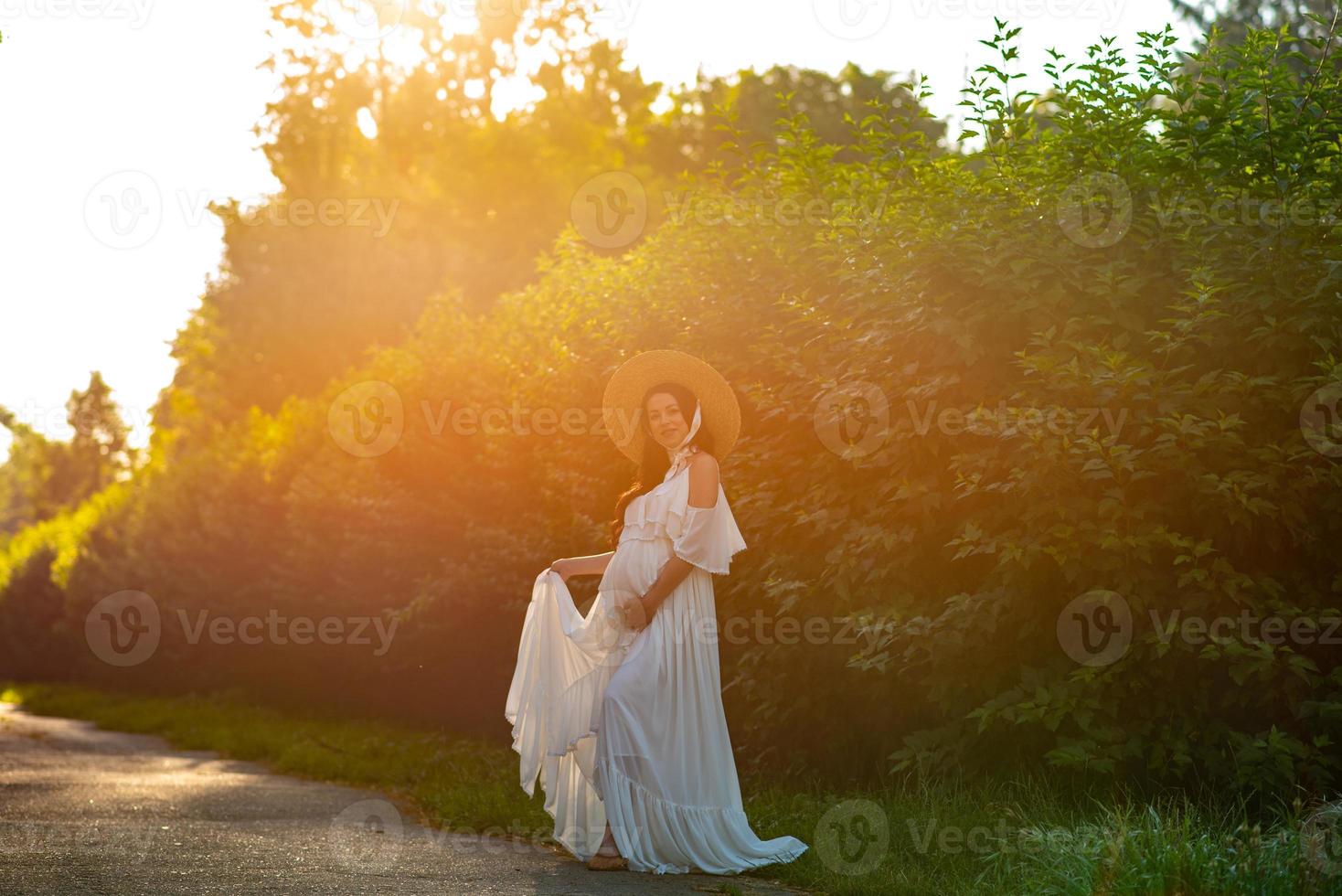 Pregnant woman in a hat posing in a dress on a background of green trees. photo