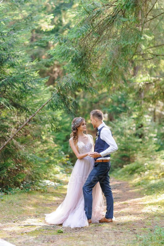 An attractive newlywed couple, a happy and joyful moment. A man and a woman shave and kiss in holiday clothes. Bohemian-style wedding cermonia in the forest in the fresh air. photo