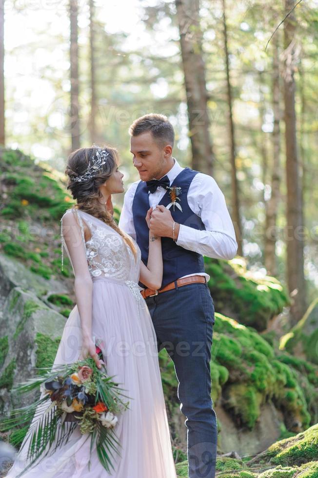 una atractiva pareja de recién casados, un momento feliz y alegre. un hombre y una mujer se afeitan y se besan con ropa de fiesta. ceremonia de boda de estilo bohemio en el bosque al aire libre. foto