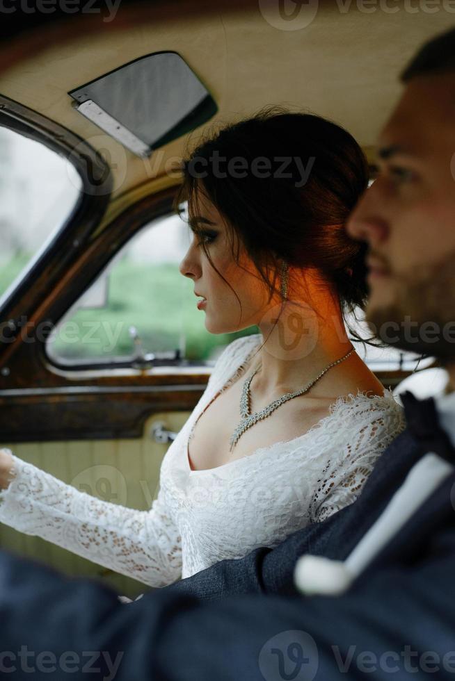 Beautiful happy young bride and groom looking from retro auto photo