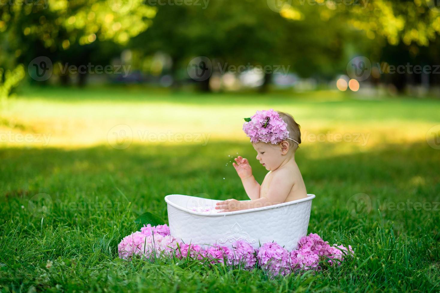 Little girl bathes in a milk bath in the park. The girl is having fun in the summer. photo