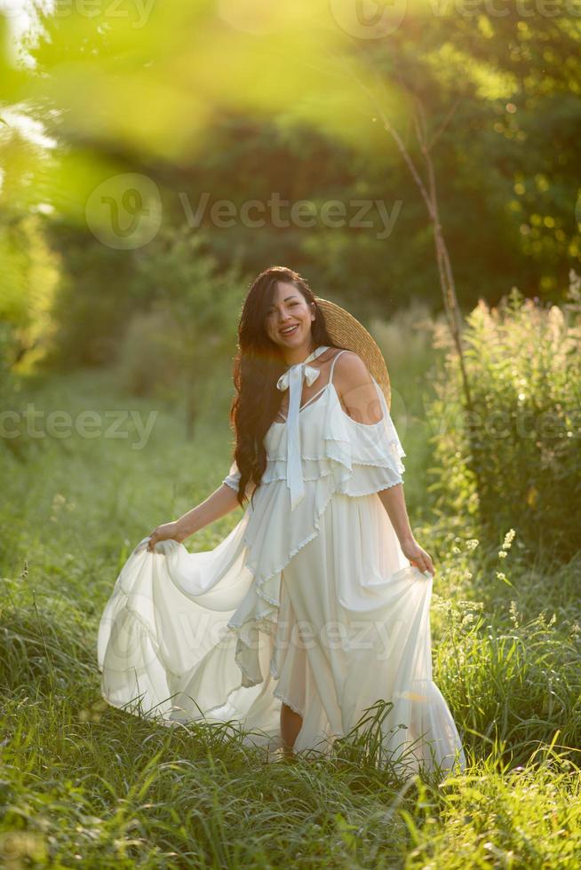 Pregnant woman in a hat posing in a dress on a background of green trees. photo