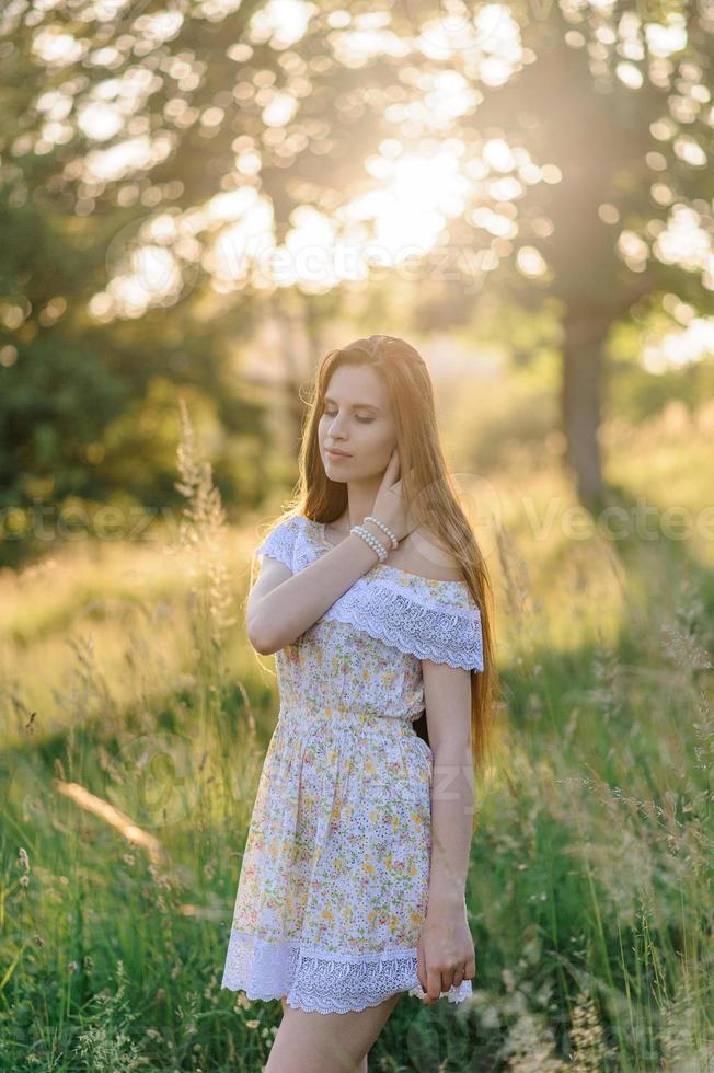 Portrait of a young beautiful girl in a sundress. Summer photo session in the park at sunset. A girl sits under a tree in the shade.