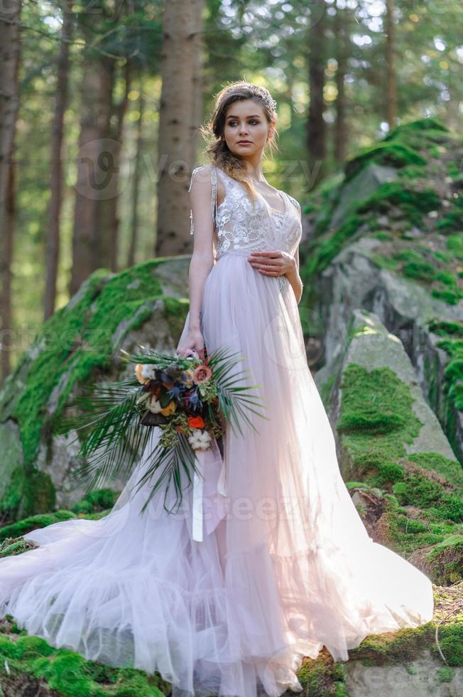 Happy bride in a pink wedding dress. The girl holds a wedding bouquet in her hands. Boho style wedding ceremony in the forest. photo