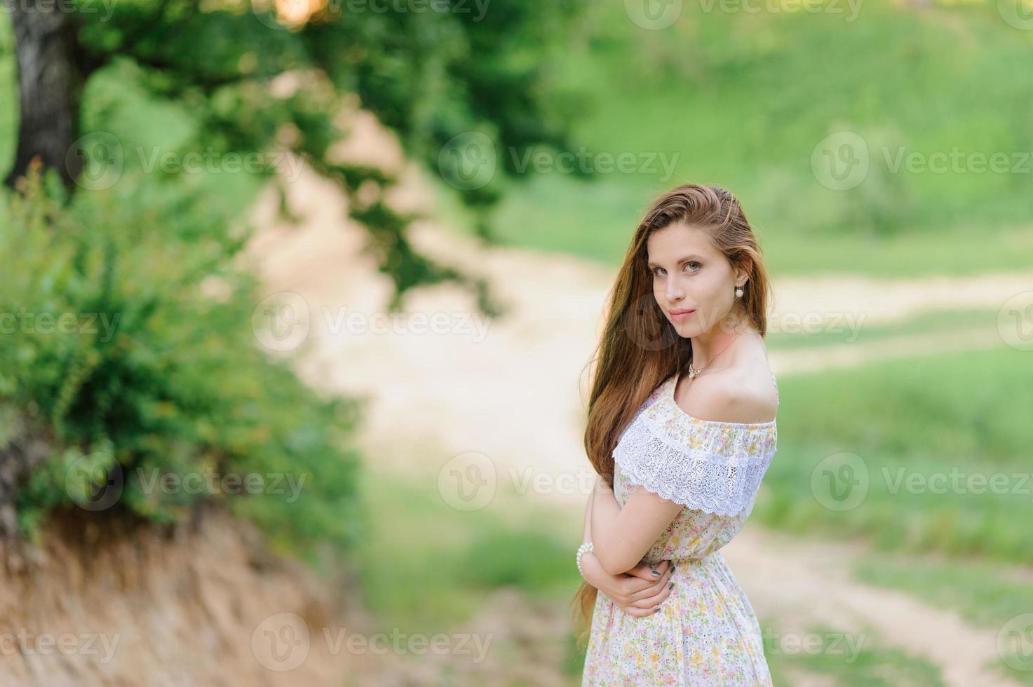 retrato de una joven hermosa en un vestido de verano. sesión de fotos de verano en el parque al atardecer. una niña se sienta debajo de un árbol a la sombra.