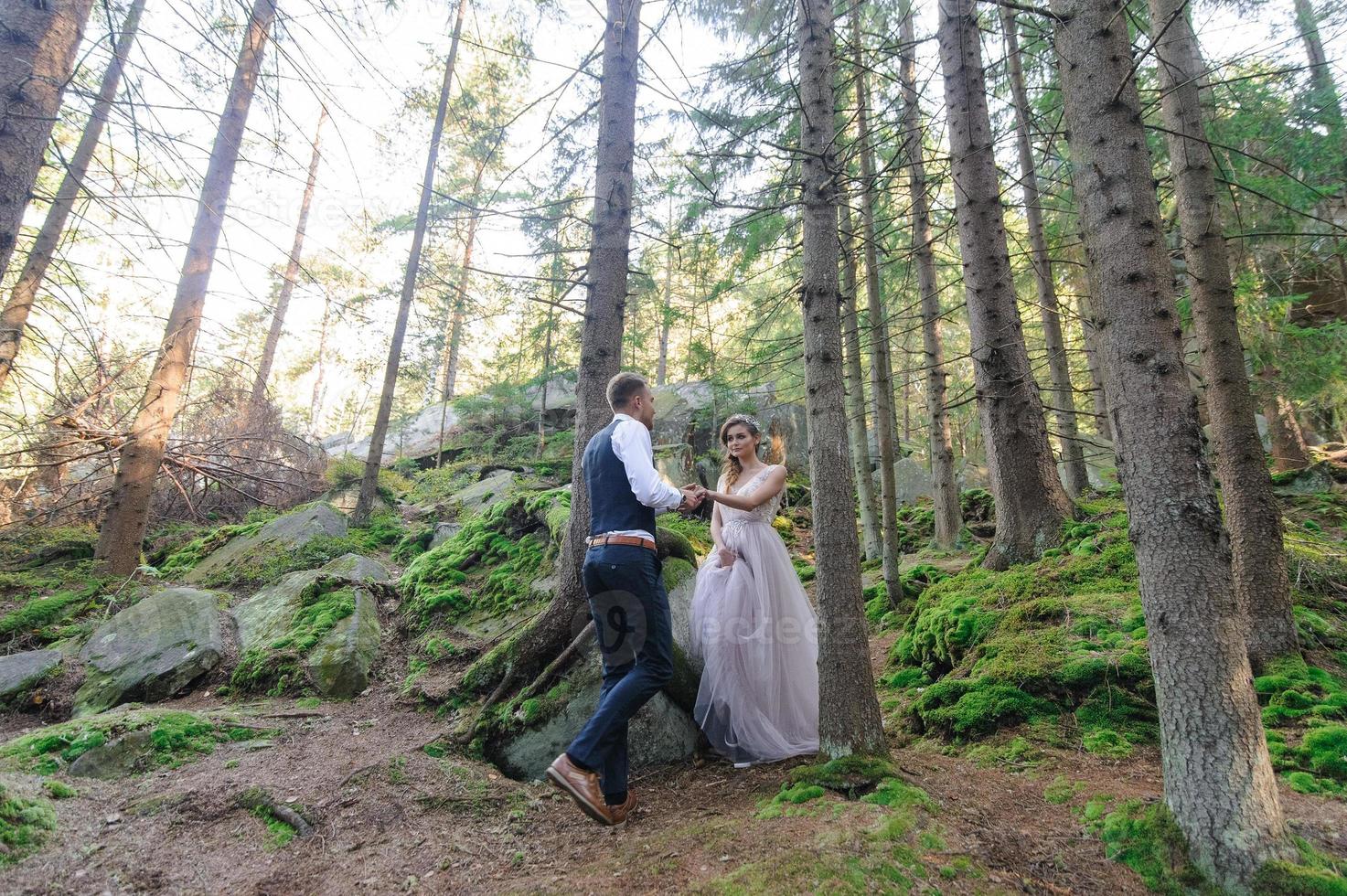 una atractiva pareja de recién casados, un momento feliz y alegre. un hombre y una mujer se afeitan y se besan con ropa de fiesta. ceremonia de boda de estilo bohemio en el bosque al aire libre. foto