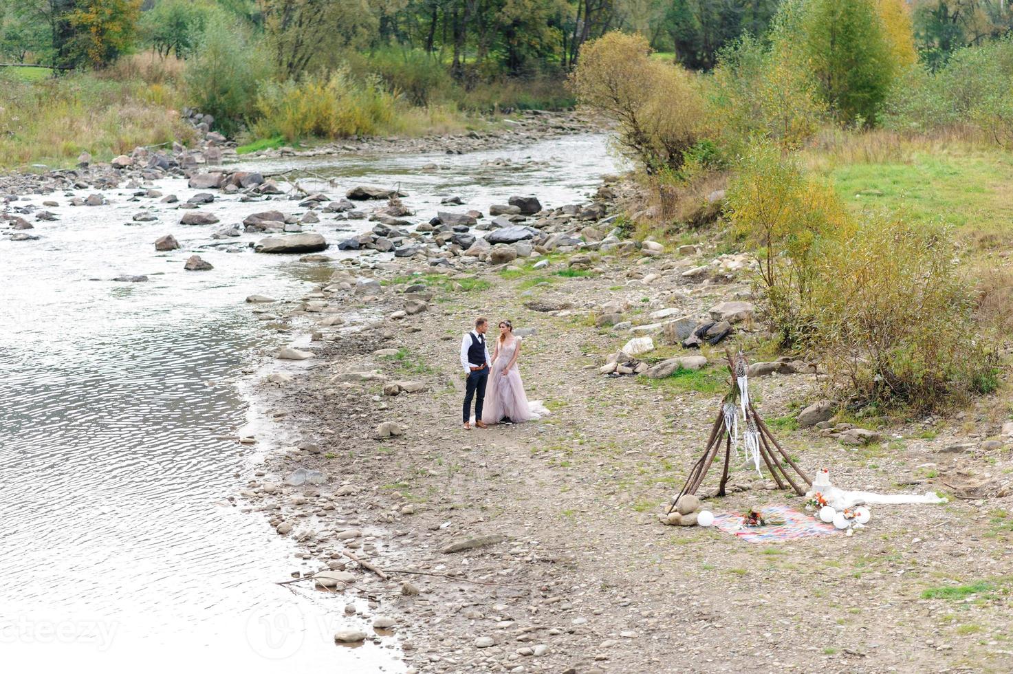 An attractive newlywed couple, a happy and joyful moment. A man and a woman shave and kiss in holiday clothes. Bohemian-style wedding cermonia in the forest in the fresh air. photo