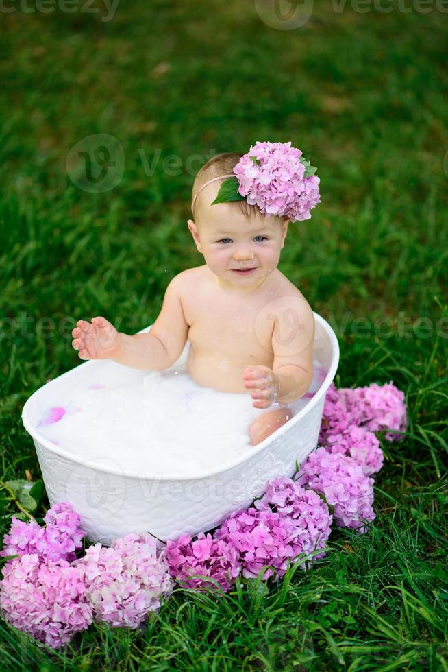 Little girl bathes in a milk bath in the park. The girl is having fun in the summer. photo