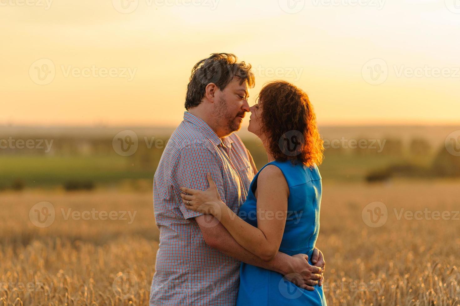 Adult farmer and wife spend time in the field. The man is sitting. A woman stands next to him and hugs him. A woman kisses her husband on the head. photo