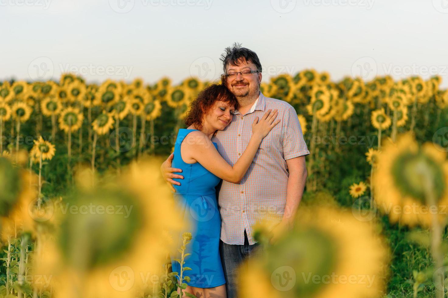 Adult farmer and wife spend time in the field. The man is sitting. A woman stands next to him and hugs him. A woman kisses her husband on the head. photo