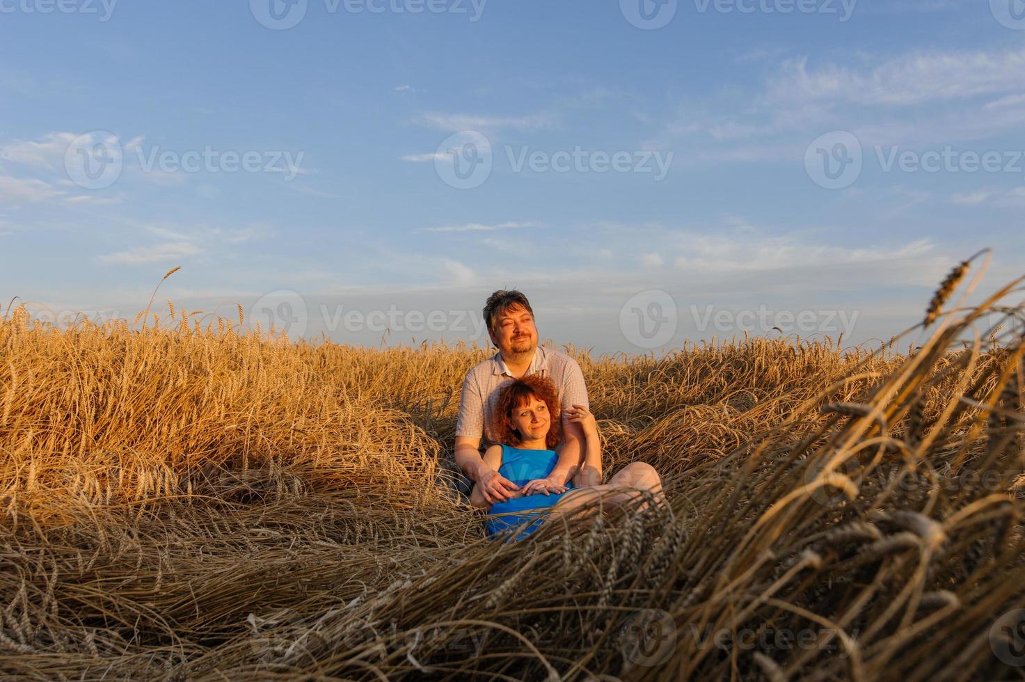 Adult farmer and wife spend time in the field. The man is sitting. A woman stands next to him and hugs him. A woman kisses her husband on the head. photo