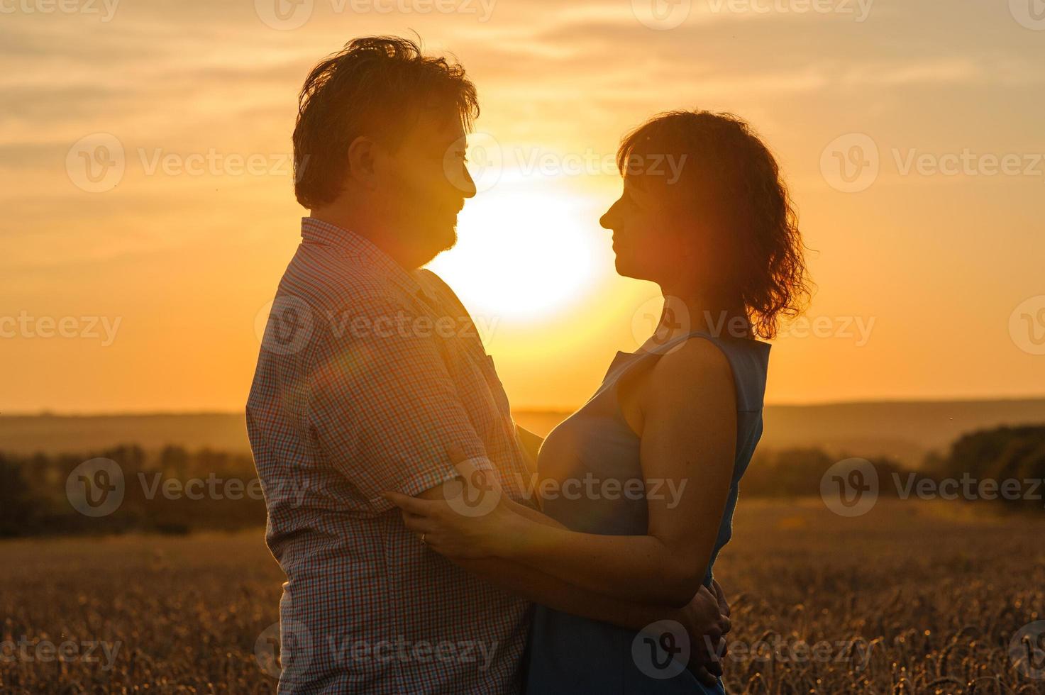 Adult farmer and wife spend time in the field. The man is sitting. A woman stands next to him and hugs him. A woman kisses her husband on the head. photo