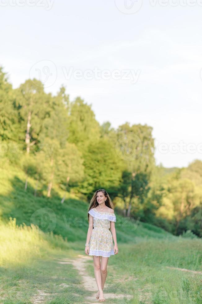 retrato de una joven hermosa en un vestido de verano. sesión de fotos de verano en el parque al atardecer. una niña se sienta debajo de un árbol a la sombra.