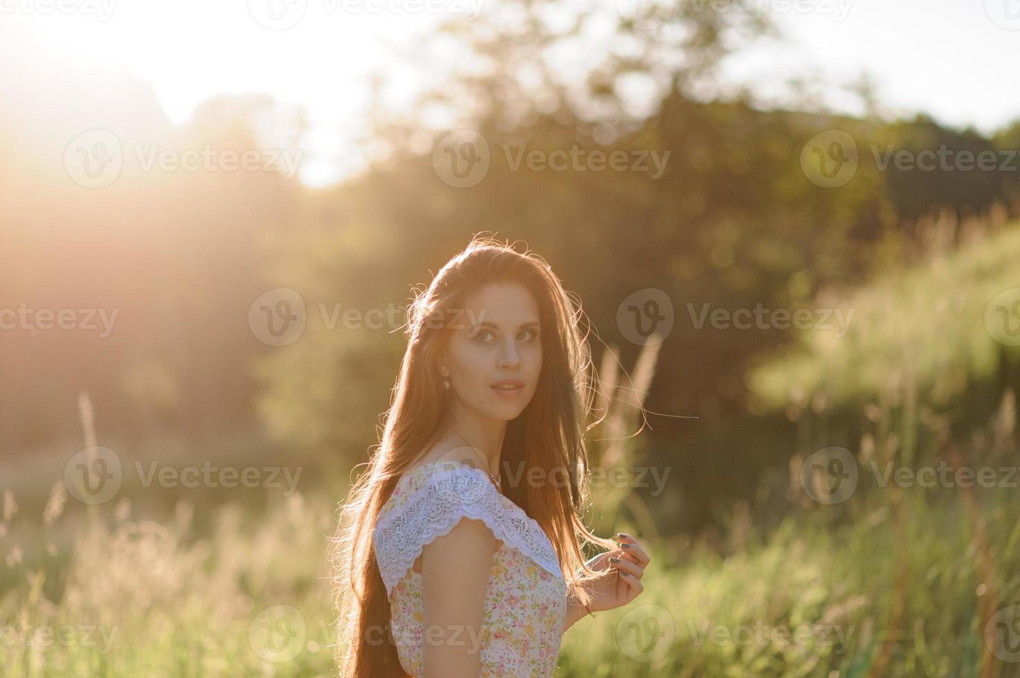 retrato de una joven hermosa en un vestido de verano. sesión de fotos de verano en el parque al atardecer. una niña se sienta debajo de un árbol a la sombra.