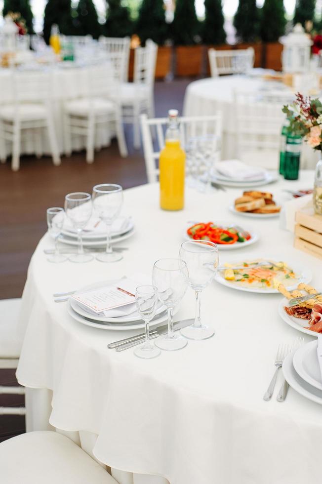 Round dinner tables covered with blue cloth stand in a white wedding pavilion photo