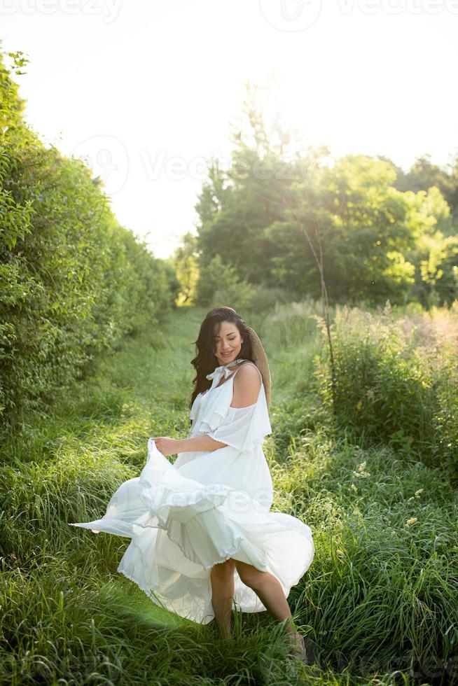 Pregnant woman in a hat posing in a dress on a background of green trees. photo