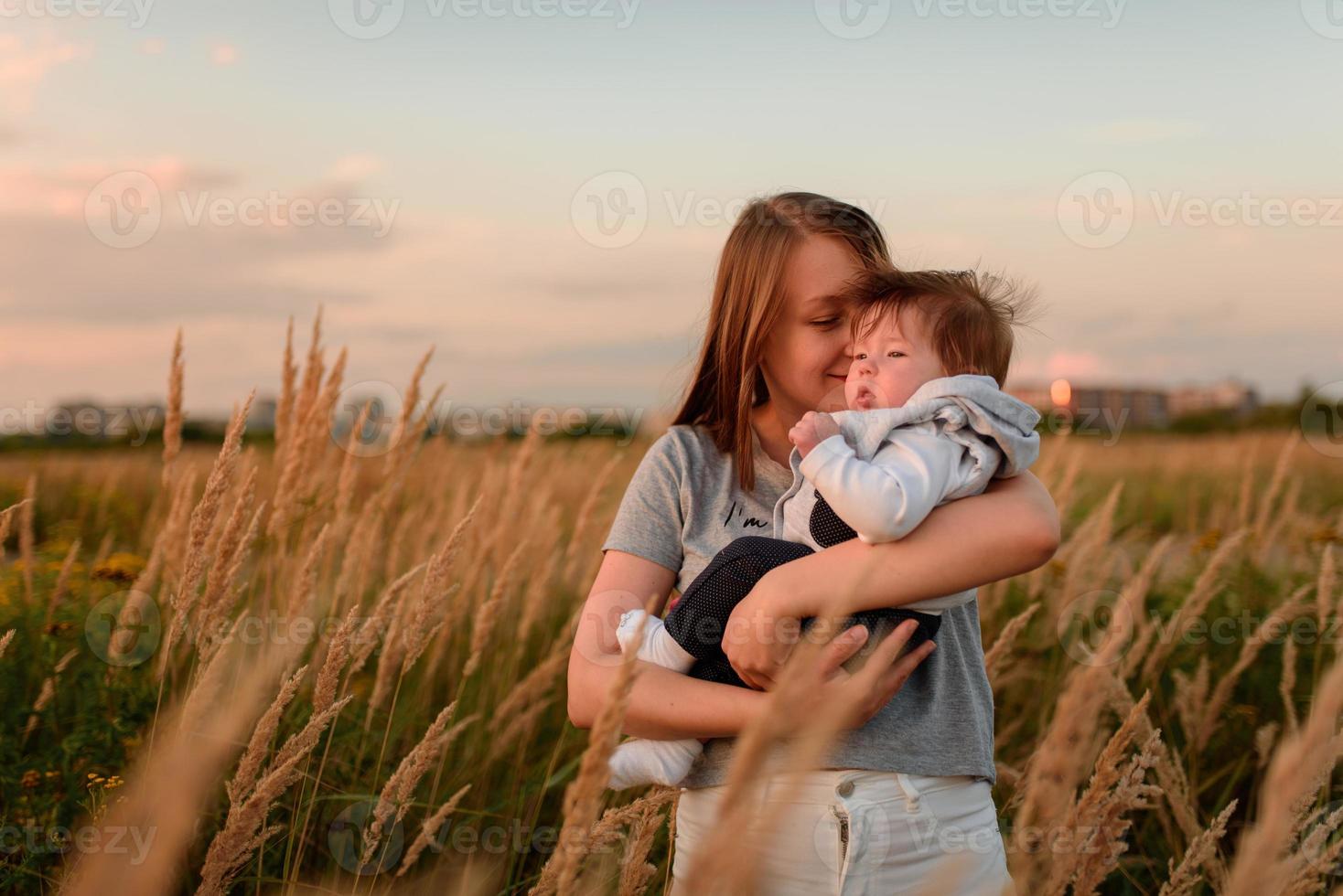 A mother walks in the field with her little daughter in her arms. photo