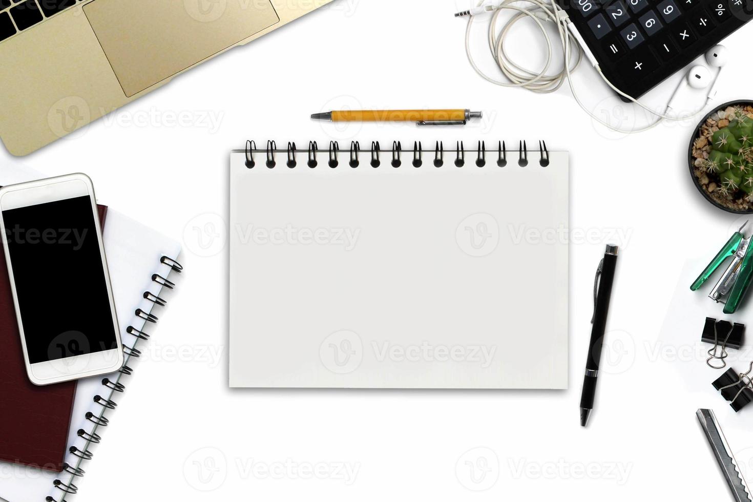 White office desk with smartphone with black screen, pen, laptop computer, notepad with copy space, and supplies. Top view with copy space photo