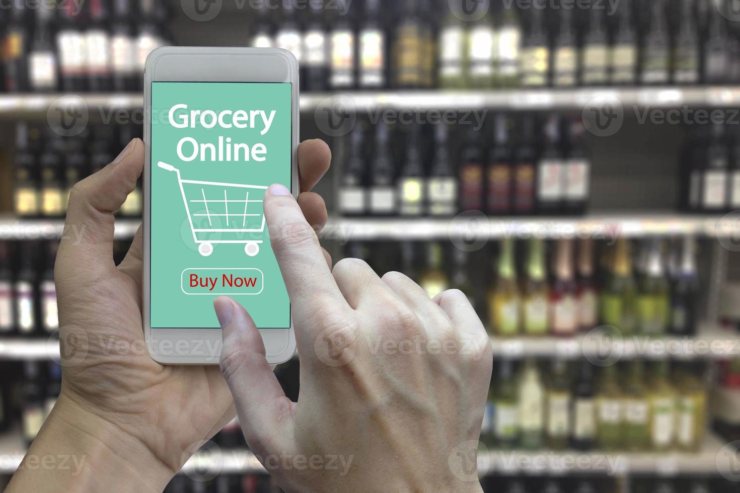 Hand use smartphone with grocery online on screen over blurred supermarket and retail store in shopping mall interior background photo