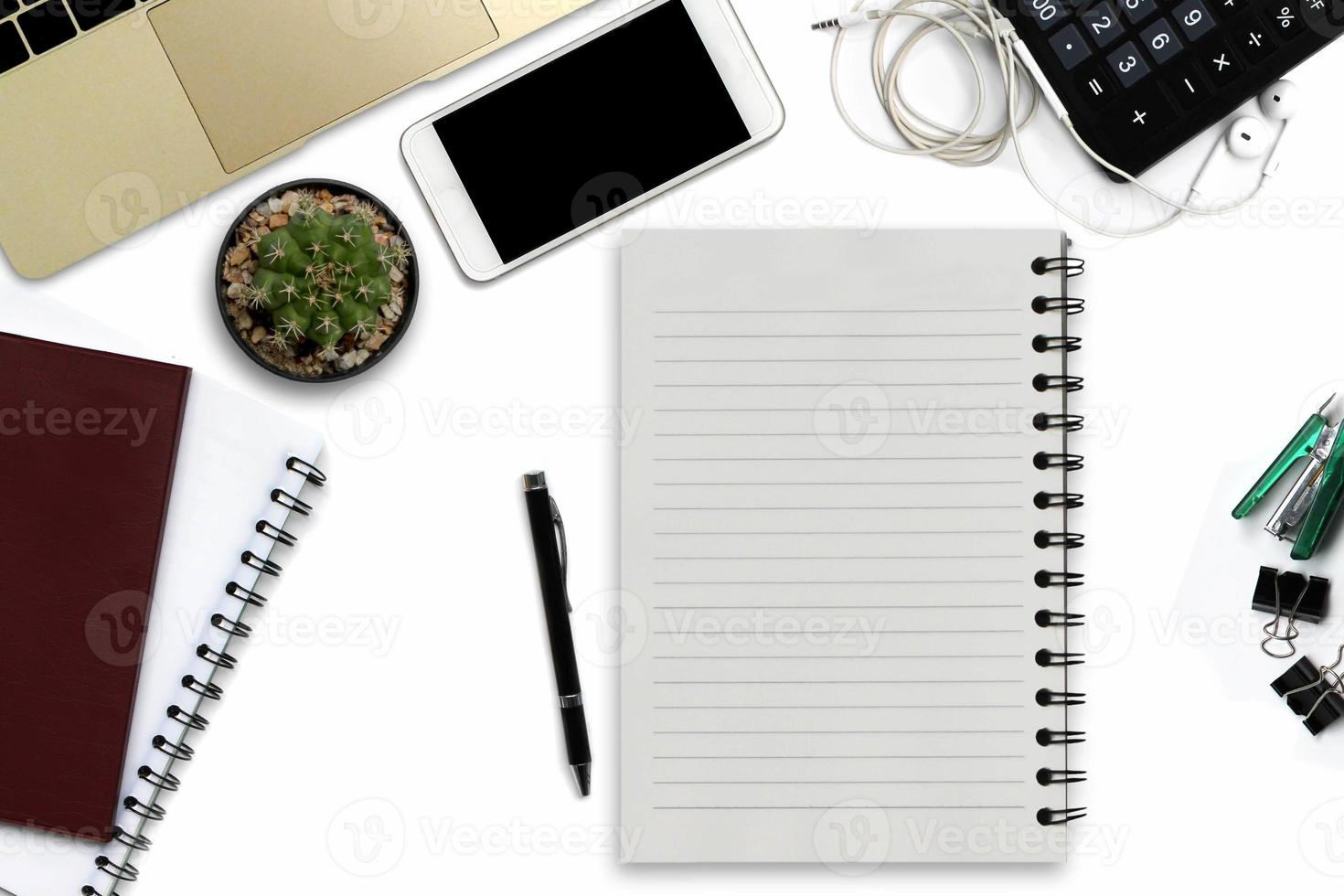 White office desk with smartphone with black screen, pen, laptop computer, notepad with copy space, and supplies. Top view with copy space photo