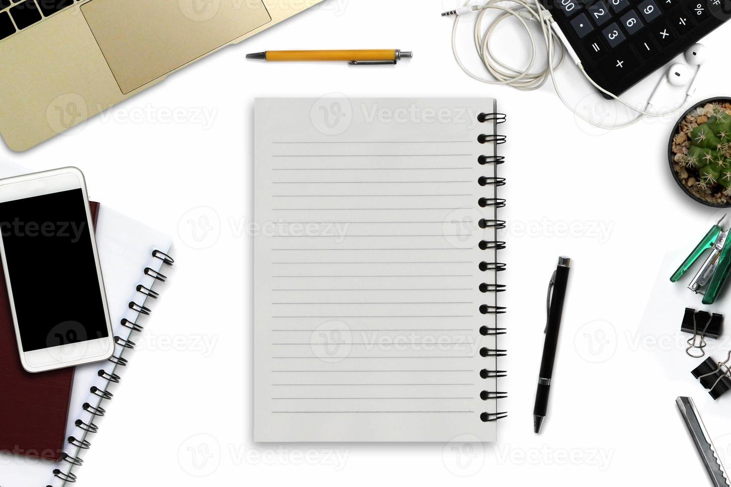 White office desk with smartphone with black screen, pen, laptop computer, notepad with copy space, and supplies. Top view with copy space photo