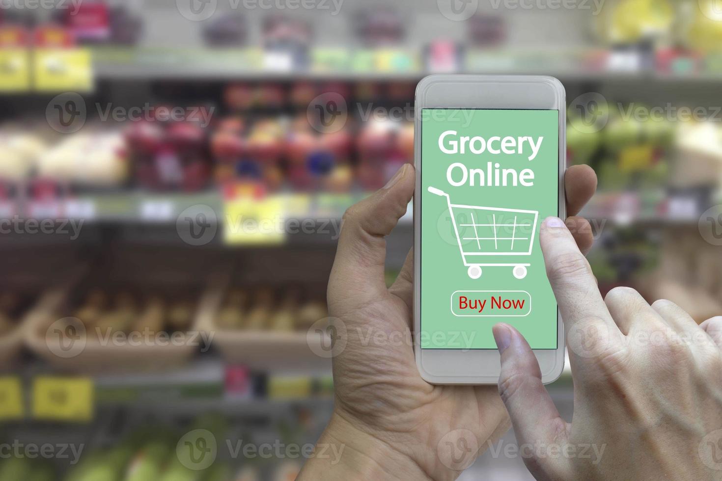 Hand use smartphone with grocery online on screen over blurred supermarket and retail store in shopping mall interior background photo