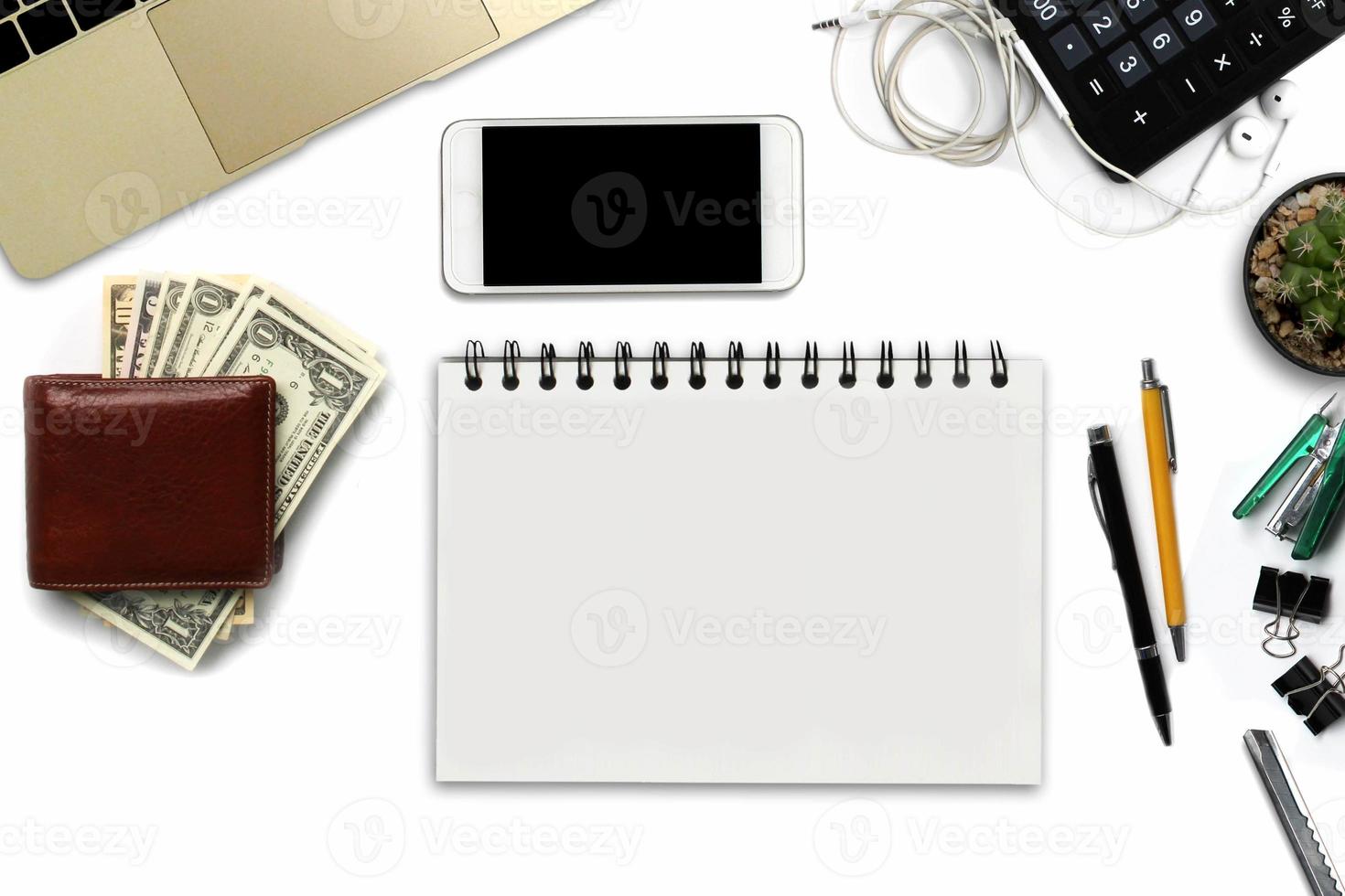 White office desk with smartphone with black screen, pen, laptop computer, wallet, and supplies. Top view with copy space photo