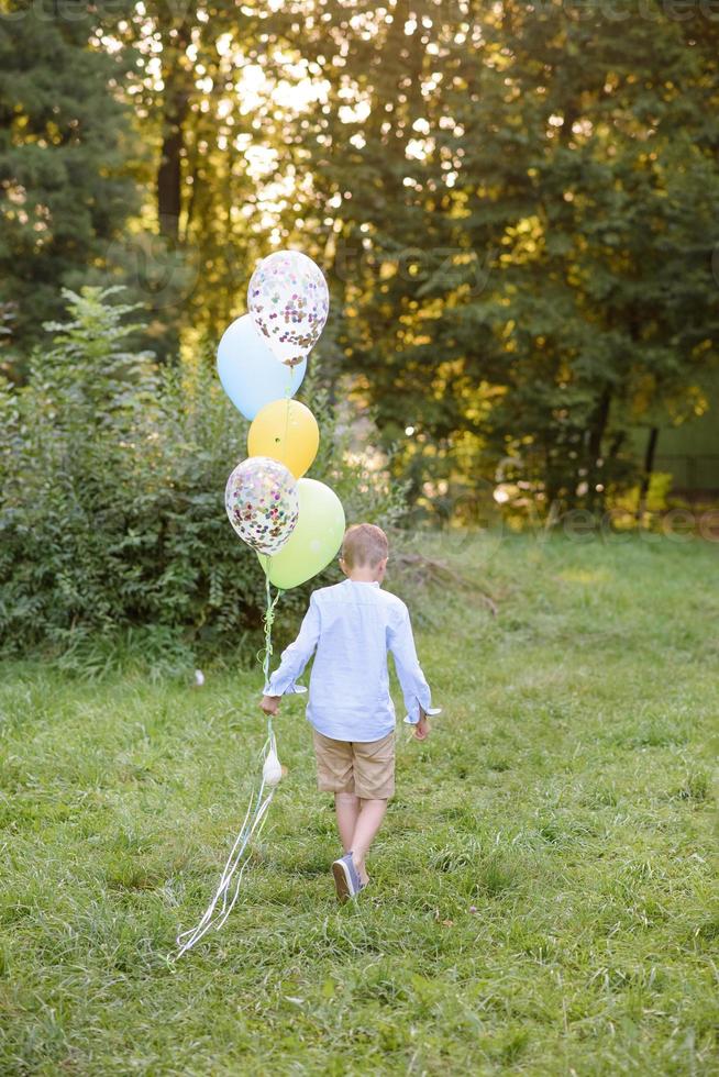 A boy of primary school age runs with balloons. The boy celebrates his birthday in the park. photo