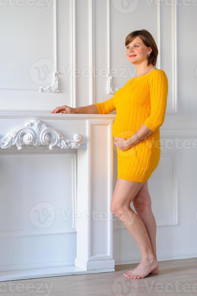 Happy pregnant woman in a yellow dress holds her belly. photo