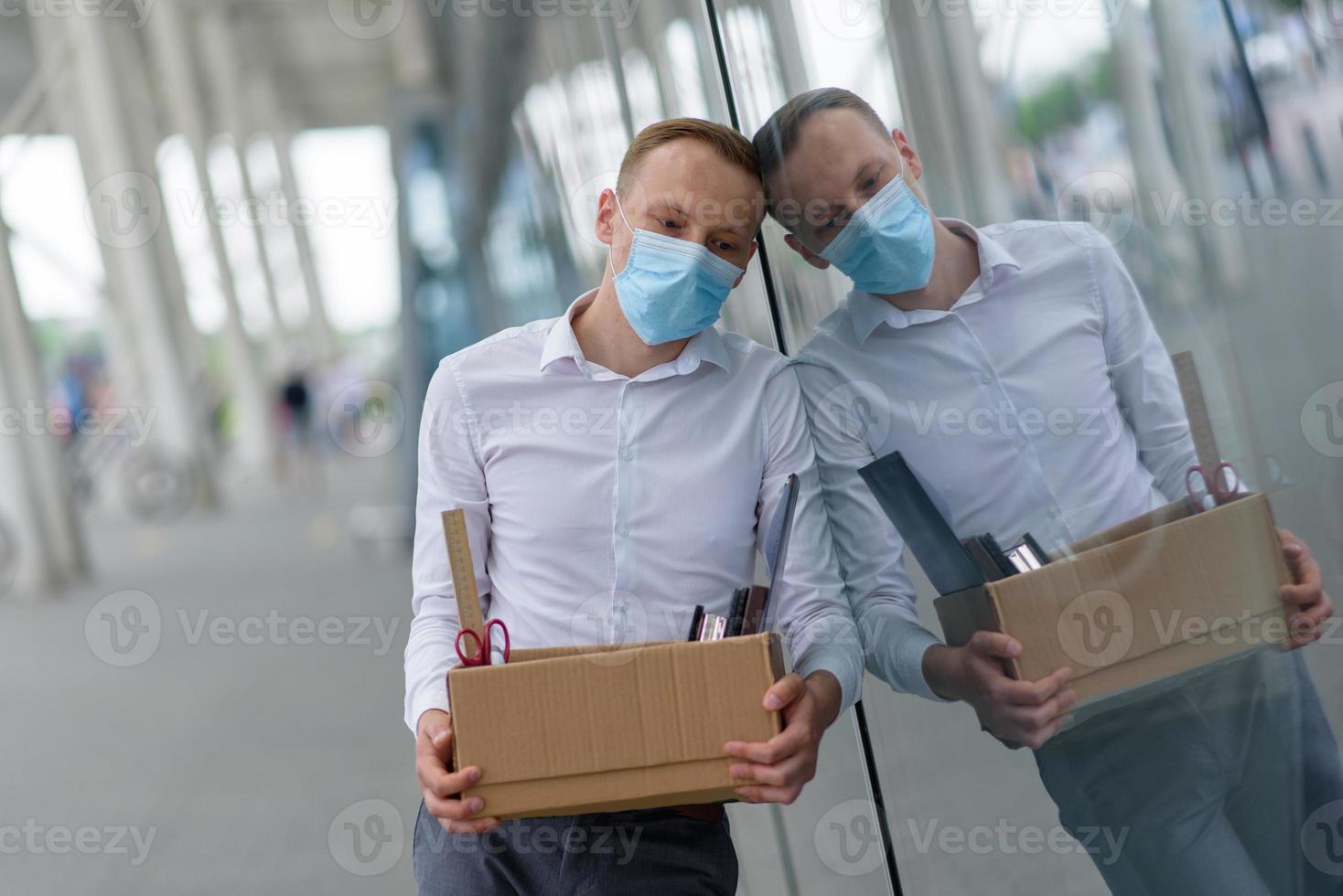 The fired office worker fell to his knees and covered his face due to stress. In front of him is a cardboard box with stationery. The man is unhappy due to a reduction in the robot. photo