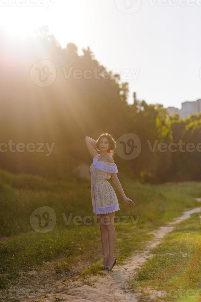 Portrait of a young beautiful girl in a sundress. Summer photo session in the park at sunset. A girl sits under a tree in the shade.