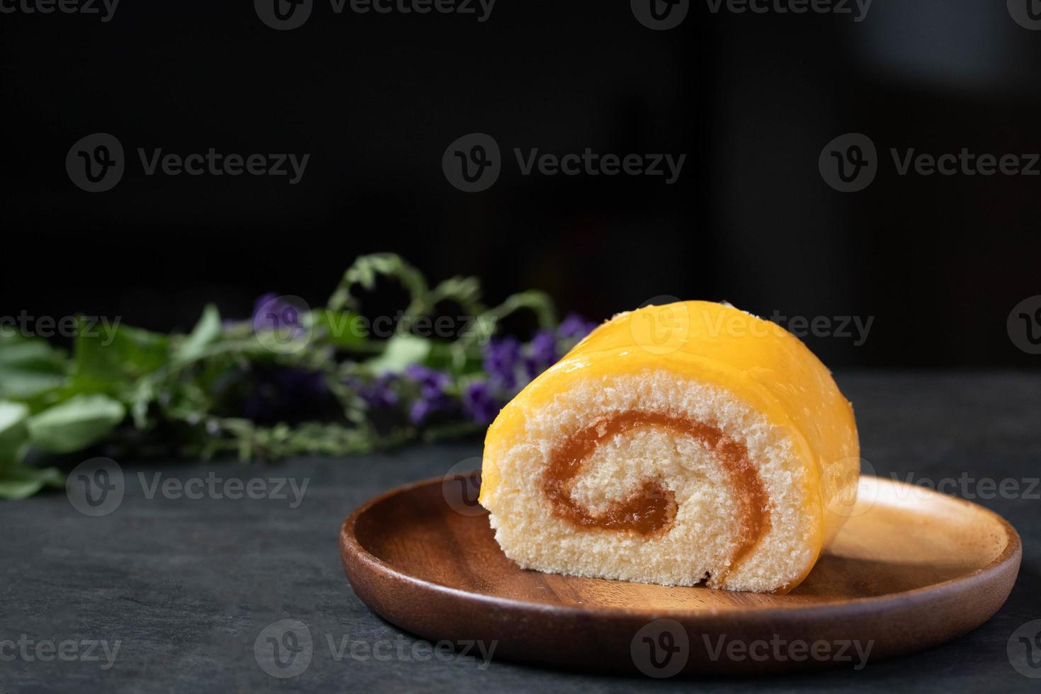 pastel de rollo de naranja en placa de madera sobre fondo negro foto