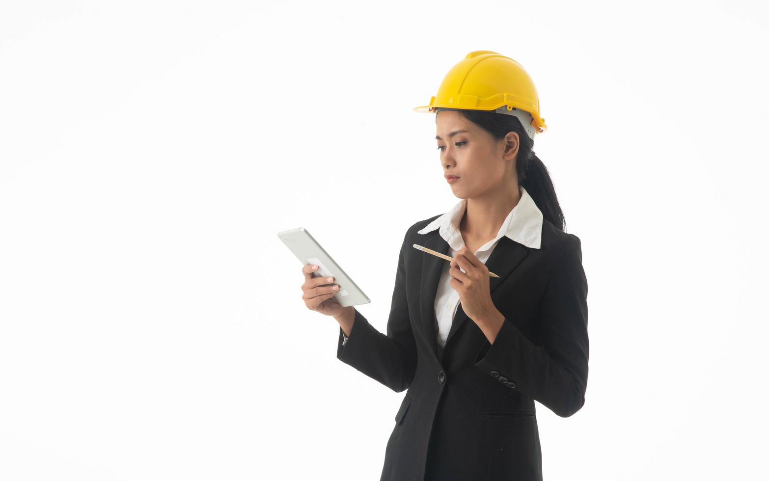 Young engineer woman wear black suit and yellow safety helmet holding note or tablet on isolated white background. photo