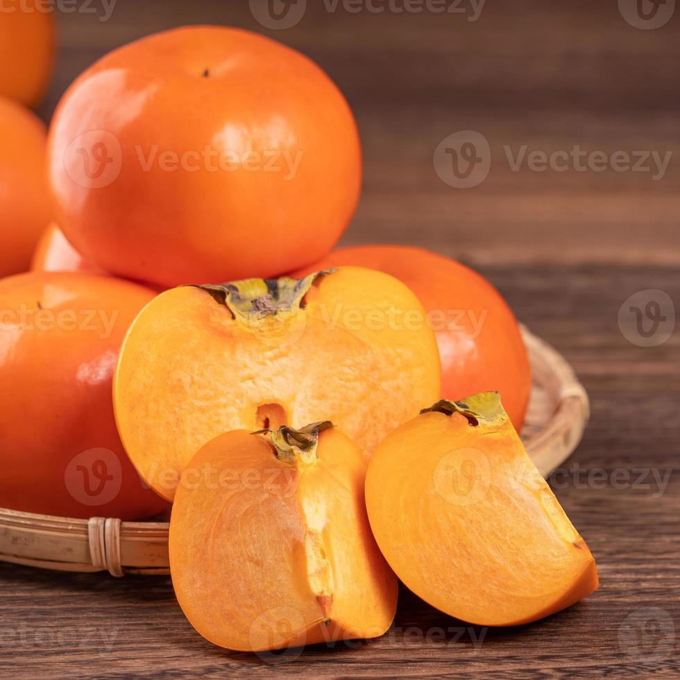 Fresh, beautiful orange color persimmon kaki on bamboo sieve over dark wooden table. Seasonal, traditional fruit of Chinese lunar new year, close up. photo