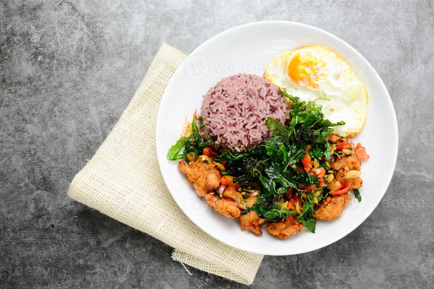 pollo crujiente cocinado con albahaca verde, servido con arroz al vapor y huevo frito, plato caliente y especiado con hojas de albahaca. foto