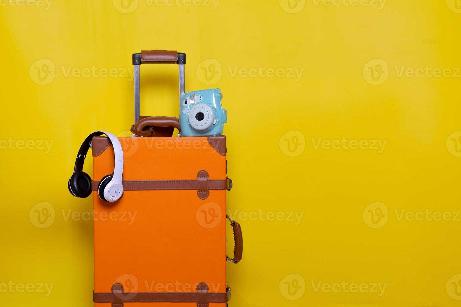 Orange suitcase with wireless headphone and mini camera isolated on yellow background for travel concept with minimal style photo