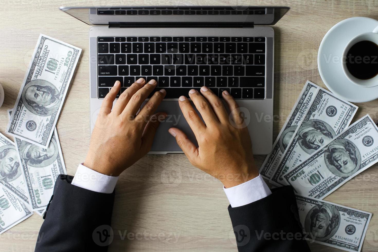 Businessman working with laptop with dollar bills around at office desk photo