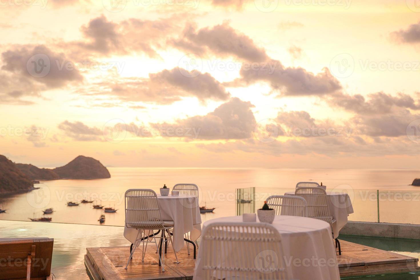 Cozy and romantic cafe with table and chairs on rooftop with sea and sunset view photo