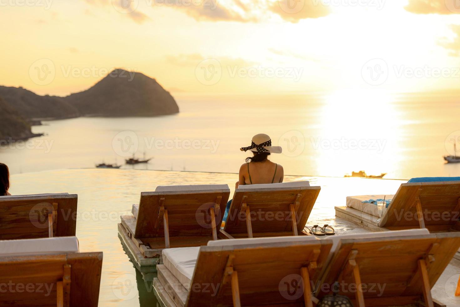 vista trasera de una mujer sentada en una silla relajante disfrutando de la puesta de sol y la vista al mar foto