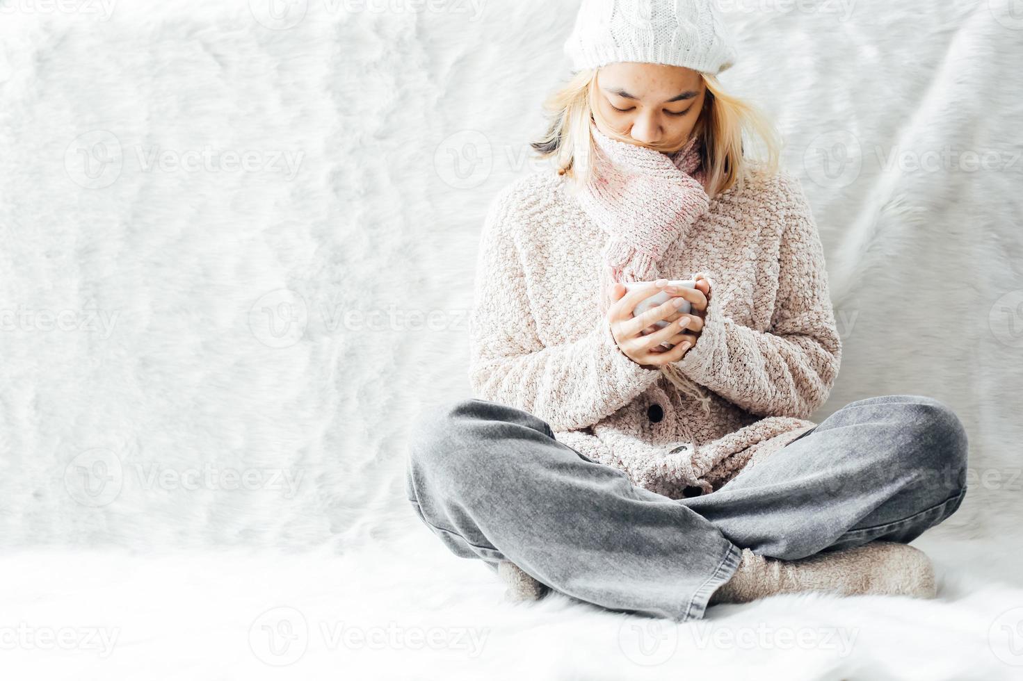 una chica con ropa de invierno disfrutando de una taza de bebida caliente en la temporada de invierno en casa foto