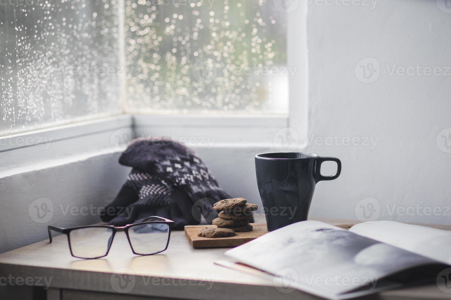 guantes de invierno y gorro con una taza de café y galletas en una mesa de madera para el fondo de invierno foto