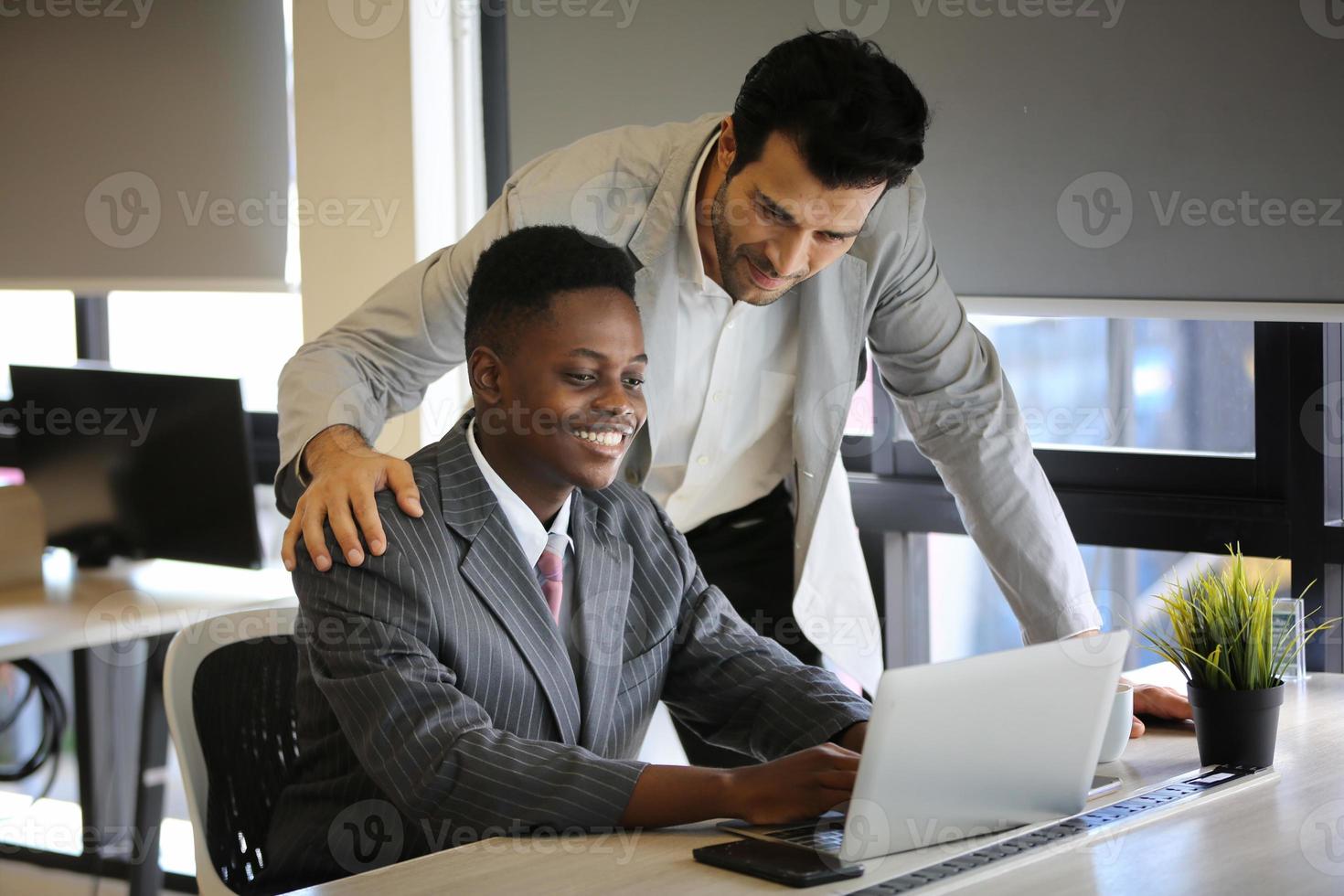 Diverse business colleagues sitting at a desk in a modern office talking together over a laptop photo