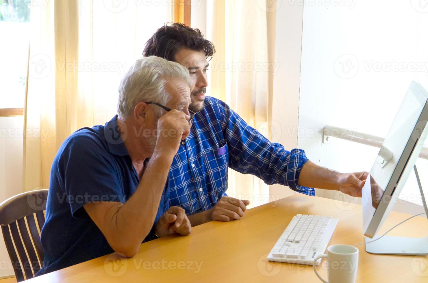young man or son teaching his grandfather elderly dad learning to using computer at home. photo