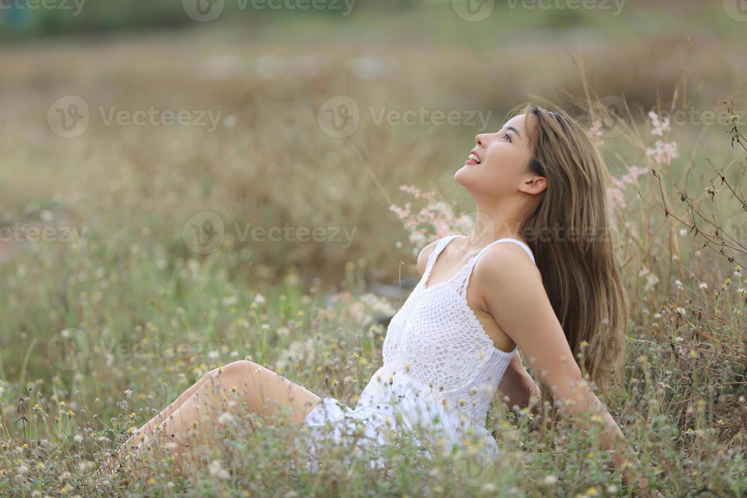 Beautiful Young Woman sitting on the field in green grass and blowing dandelion. Outdoors. Enjoy Nature. Healthy Smiling Girl on spring lawn. Allergy free concept. Freedom photo