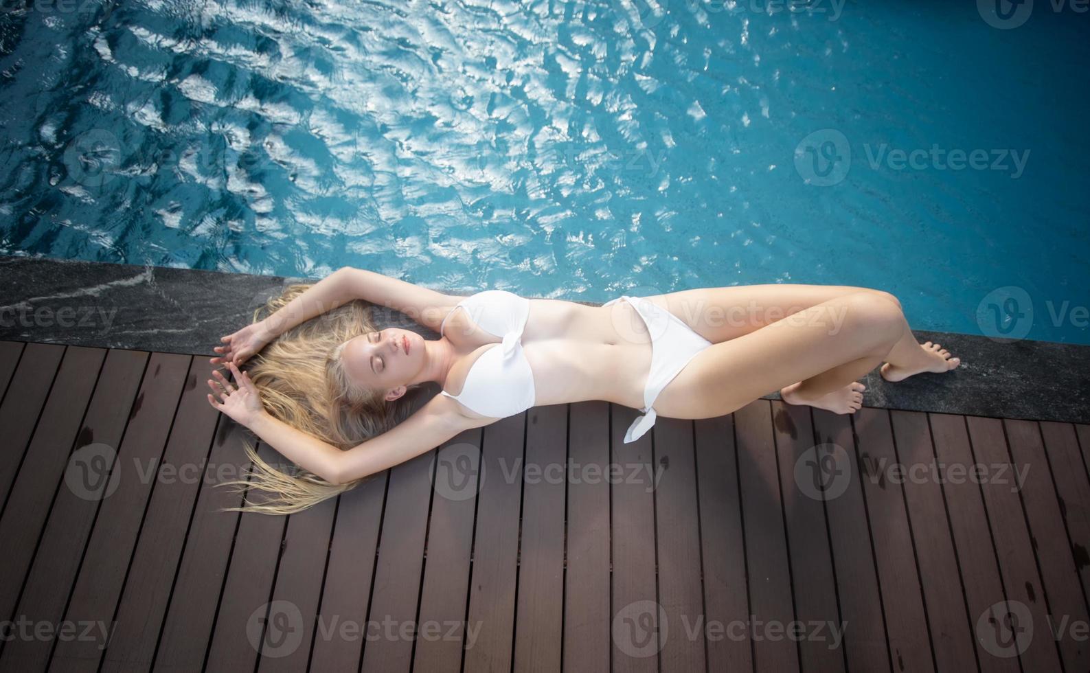 woman in white bikini tanning by the pool photo